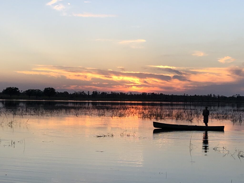 a person in a canoe fishing on a lake at sunset